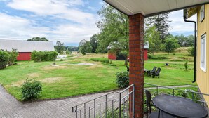 Un espace extérieur abrité, doté d’une colonne en briques, d’un chemin pavé et offrant une vue sur un champ verdoyant avec une grange rouge et des arbres.