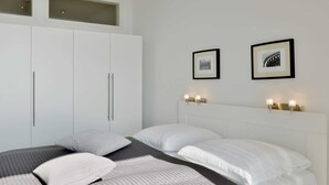 Un dormitorio moderno con una cama grande, un armario blanco y dos lámparas fijadas a la pared.