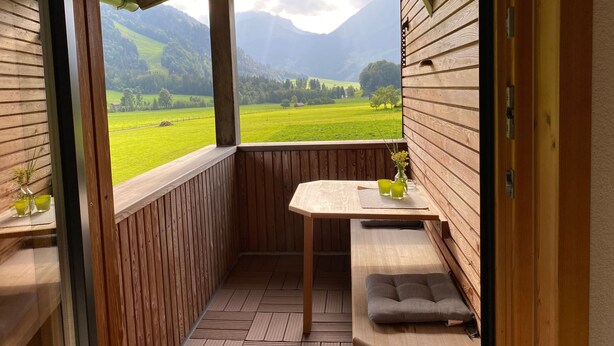 Ein Holzbalkon mit Tisch und Bank, mit Blick auf ein grünes Tal und Berge.