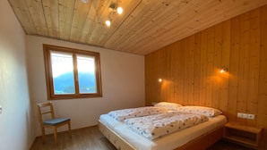 Ein Schlafzimmer mit Holzboden, einem Bett mit floralem Bettzeug, einem Stuhl und einem Fenster mit Blick.