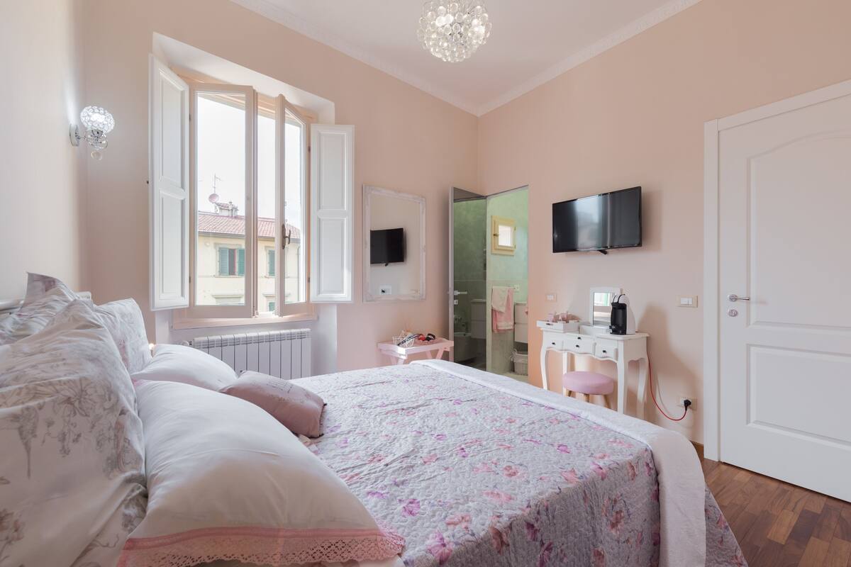 A bedroom with a bed, a desk, a mirror, and a TV.