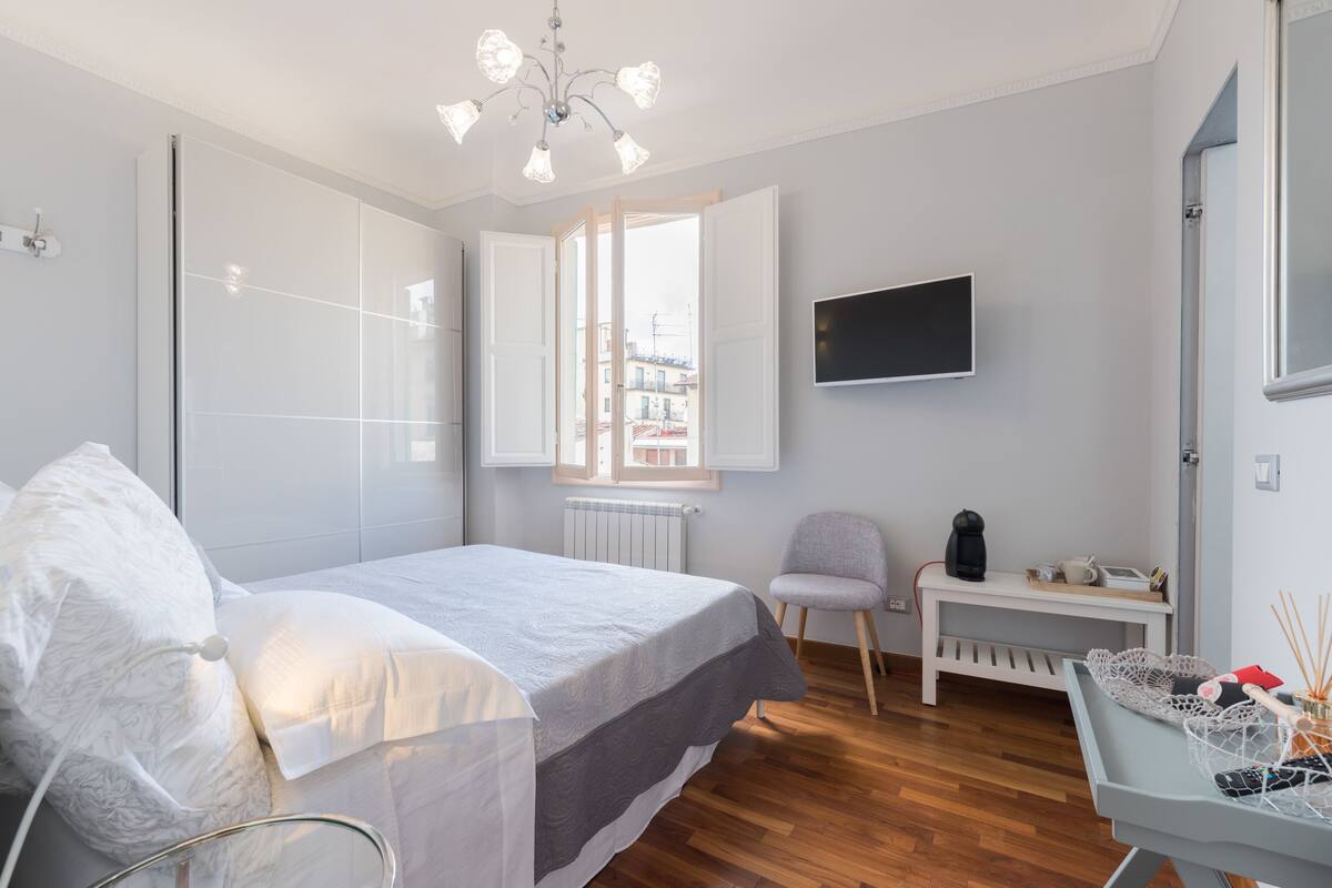A modern bedroom with a bed, a chair, a desk, and a TV.