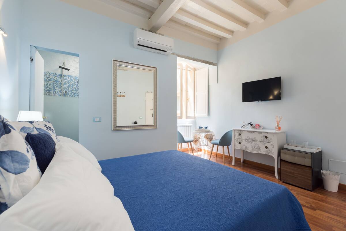 A bedroom with a bed, a dresser, a TV, and a bathroom visible through an open door.