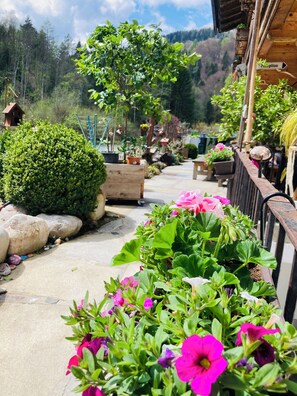 Stroll through the serene garden pathway to a charming wooden building surrounded by lush greenery and vibrant flowers.
