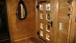 A wooden interior with a door featuring a window, a mirror, and a light switch.