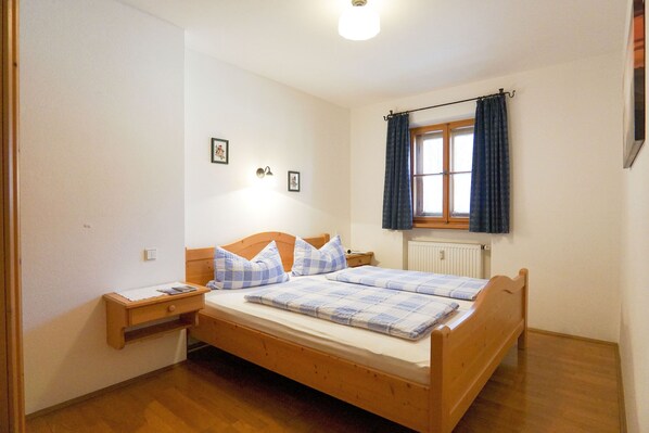 Un dormitorio con cama de madera, una mesita de noche, una ventana con cortinas y una lámpara de pared.
