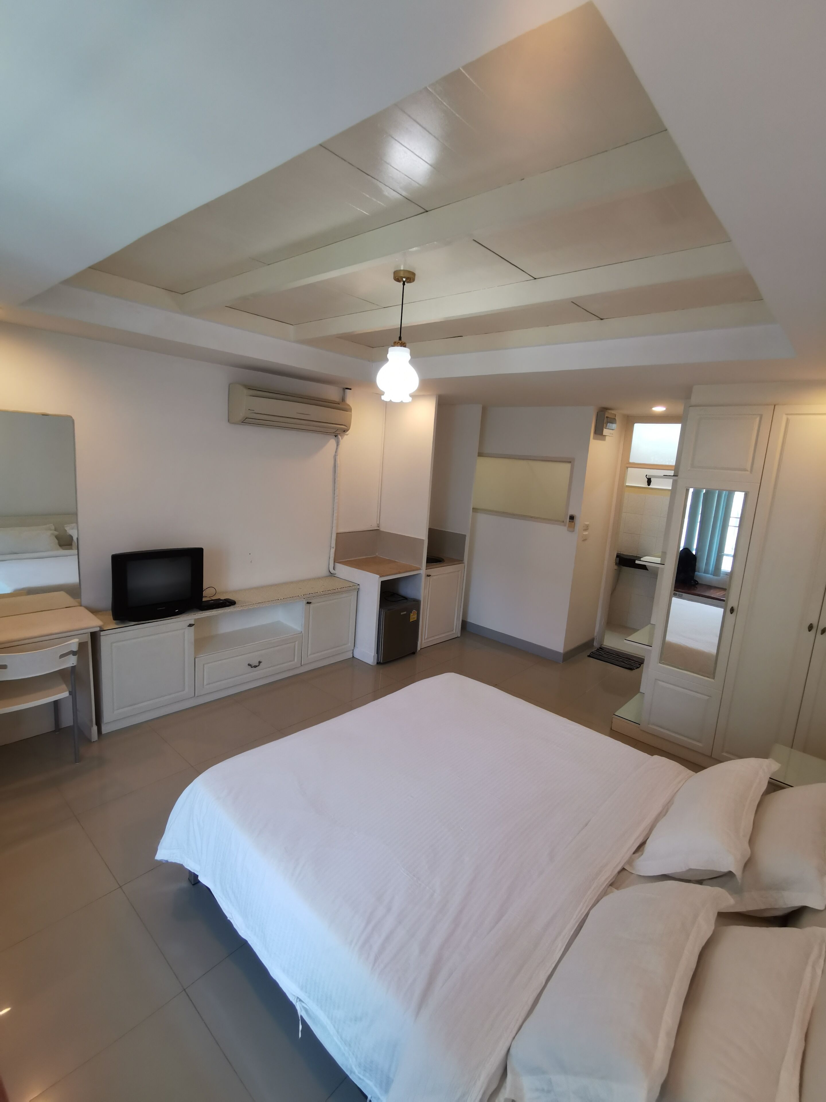 Une chambre comprenant un lit, un bureau, une télévision, un appareil de climatisation et une armoire.