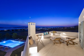 A rooftop terrace with a pool, outdoor seating, and a view of the city at dusk. - Villa Vesper Paros (Paros)