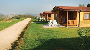A row of wooden cabins with a dirt path leading to them, surrounded by green fields and hills. - Lovely home in Gerolstein with WiFi (Gerolstein)