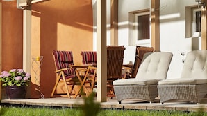 Eine überdachte Terrasse mit Korbmöbeln, einem Blumentopf und einem Holzstuhl.