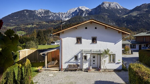 Ein weißes, zweistöckiges Haus mit geneigtem Dach, einer überdachten Veranda und einem kleinen Garten.