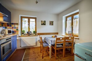 Une cuisine compacte avec un coin repas, des meubles en bois, un réfrigérateur de style vintage et une fenêtre avec des rideaux.