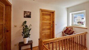 Eine Holztreppe mit Geländer, ein Blumentopf, eine Holztür und ein Fenster mit Blick auf Blumen.