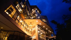 Un immeuble moderne  à plusieurs étages, doté de grandes fenêtres et de balcons, et caractérisé par un luminaire central imposant.