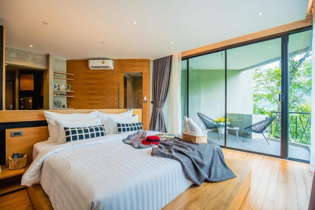 Ein modernes Hotelzimmer mit einem großen Bett, einem Balkon mit einem Stuhl und Blick ins Grüne.