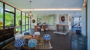 Un vaste espace de vie agrémenté d’une grande fenêtre, d’une table à manger en bois et de poufs bleus à motifs.