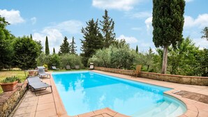 Ein rechteckiger Pool mit Steinbordstein, umgeben von einer Terrasse mit Liegestühlen und einer Steinmauer.