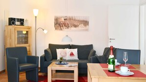 A living room with a sofa, two armchairs, a coffee table, a dining table with a bottle of champagne and a glass, and a lamp. - Bernstein Suite—right on the beach! - Bernstein Suite (Glowe)