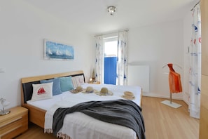 A neatly arranged bedroom with a bed, bedside tables, a nightstand, a window with curtains, a painting on the wall, and a hat rack.