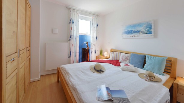A bedroom with a wooden wardrobe, a bed with a red blanket, two hats, and a painting on the wall. - Bernstein Suite—right on the beach! - Bernstein Suite (Glowe)