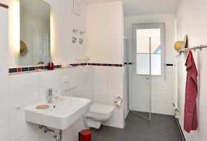A modern bathroom with a white sink, toilet, and shower area.