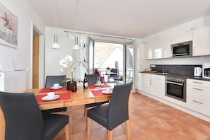 A modern kitchen with white cabinets, a built-in oven, and a dining area with a red placemat.