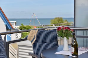 A balcony with a view of the sea, a table with a bottle of wine, and a vase of flowers.