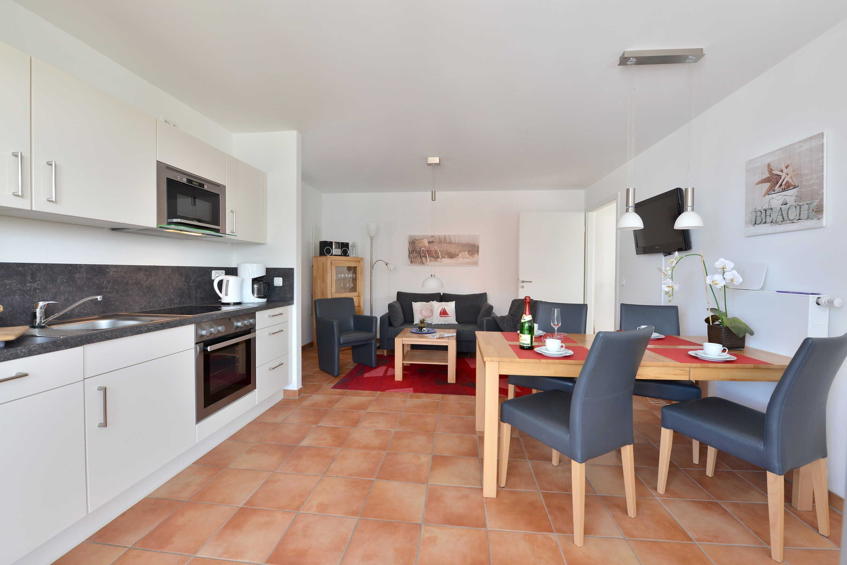 A modern kitchen with white cabinets, a built-in oven, and a black countertop. There is a dining area with a wooden table and blue chairs.
