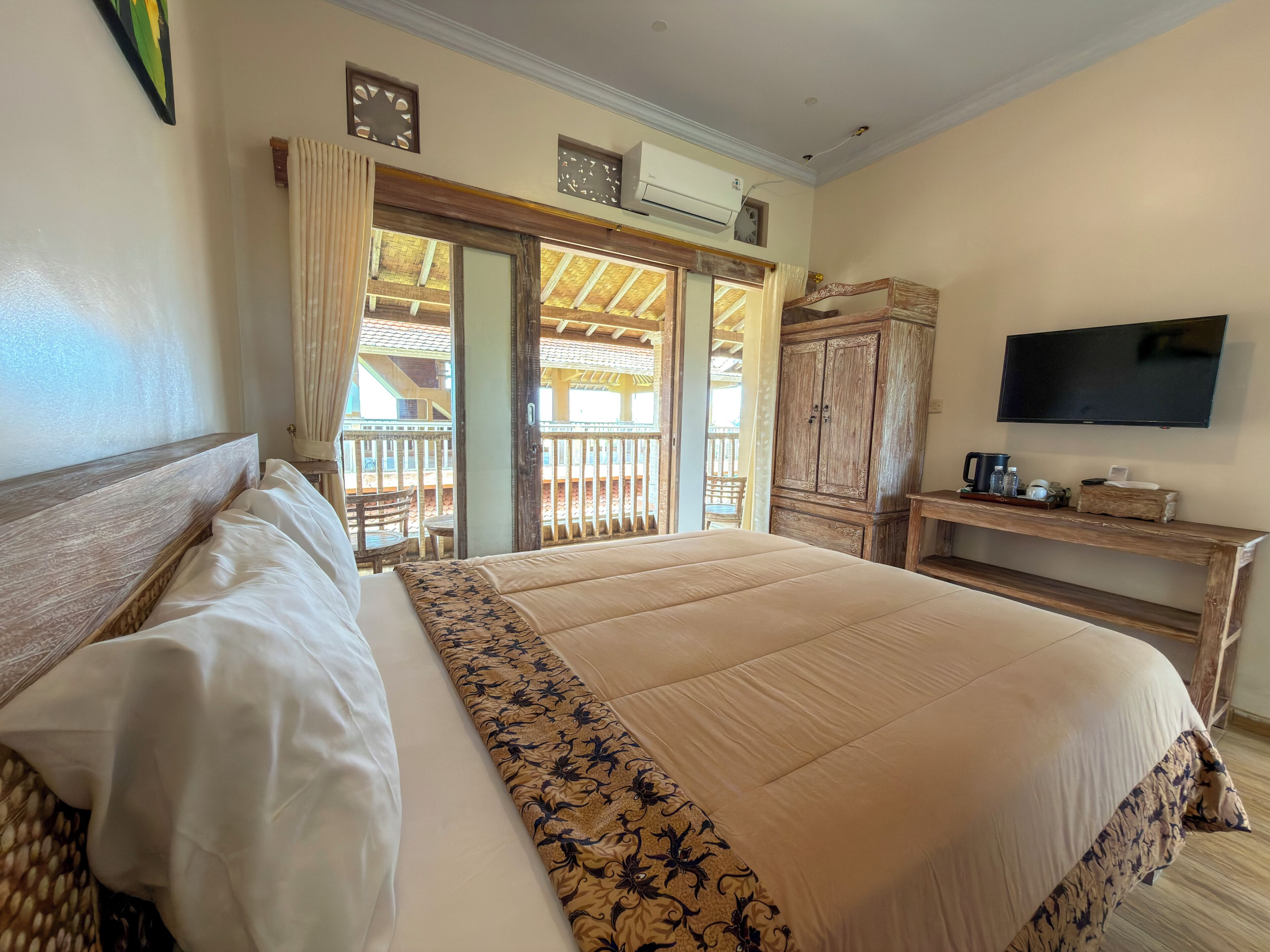 Habitación de hotel con una cama grande, cabecera de madera, televisión, escritorio con cafetera y balcón con barandilla de madera.
