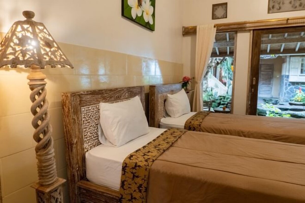 A hotel room with two beds, a decorative lamp, and a view of a garden through a sliding door.