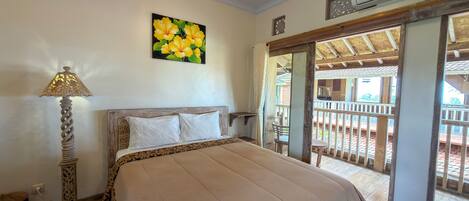 A bedroom with a bed, a painting of flowers, an air conditioning unit, and a balcony with a view.