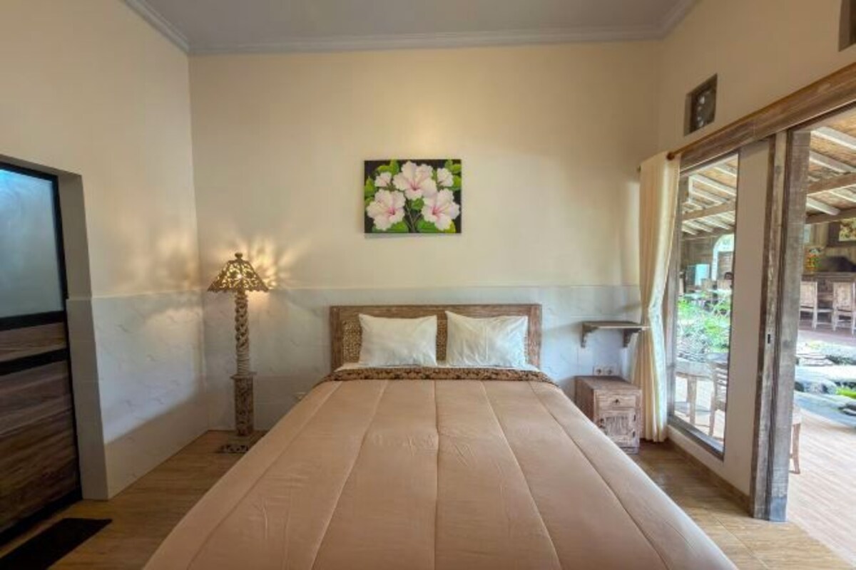 Une chambre à coucher avec un lit, une lampe, un tableau et une vue sur l’extérieur.