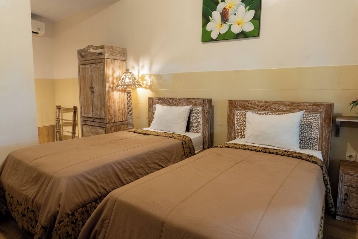 A hotel room with two beds, a wooden wardrobe, a mirror, and a wall-mounted lamp.