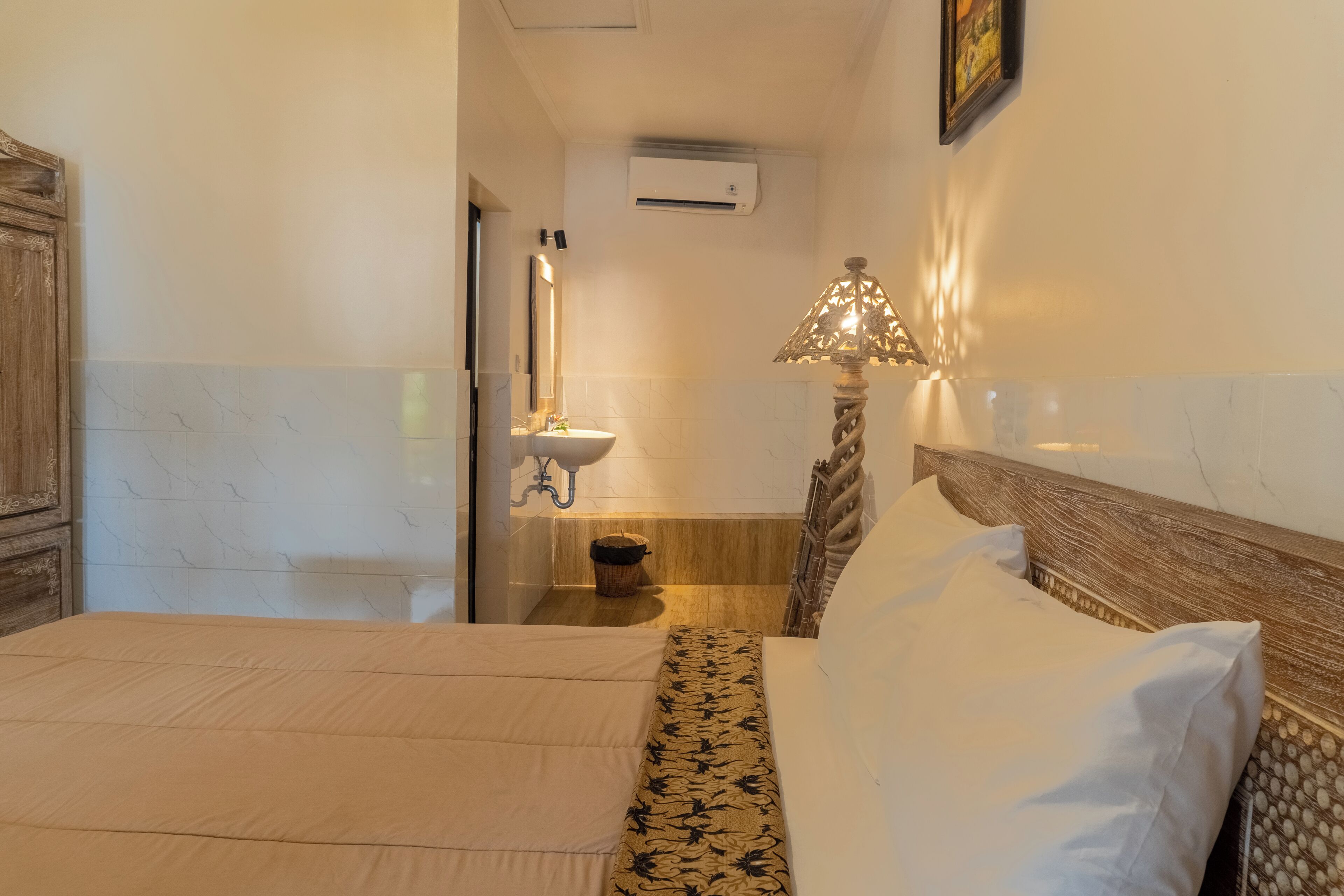 Un dormitorio con cama, mesita de noche, lámpara y baño con lavamanos y espejo.