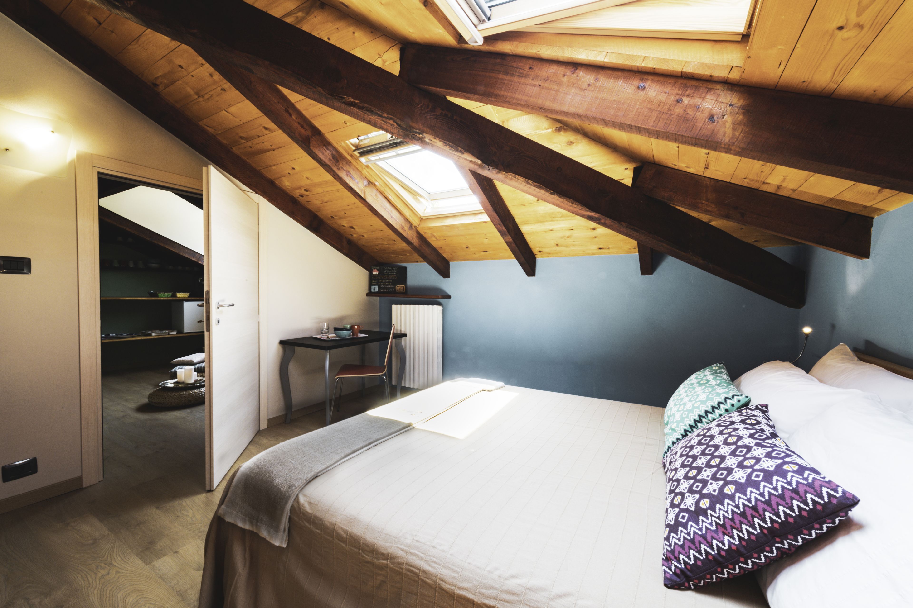 A bedroom with a sloped ceiling, a bed with patterned pillows, a desk with a chair, and a skylight.