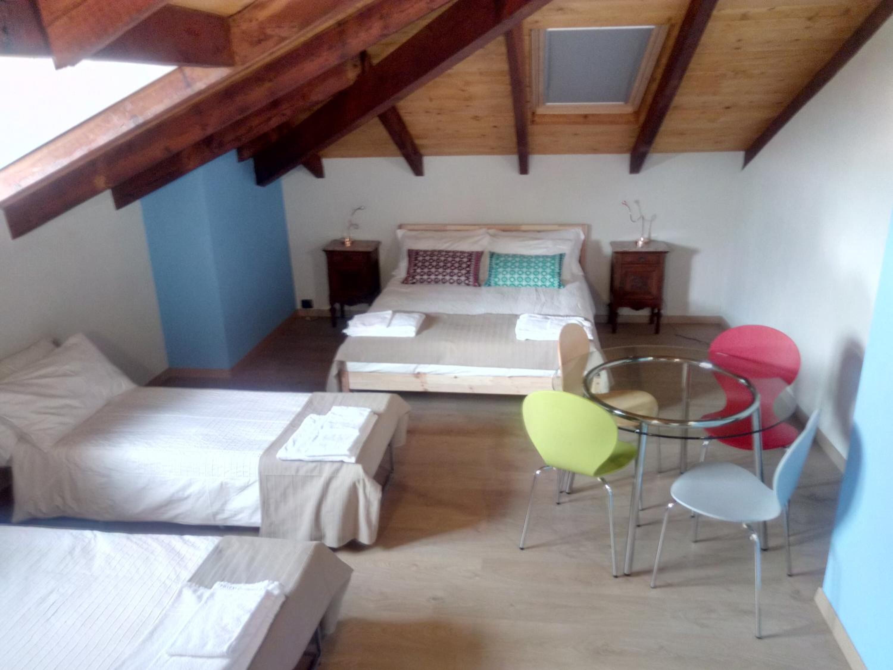 A bedroom with a loft-style ceiling, a bed, two bedside tables, and a small table with chairs.
