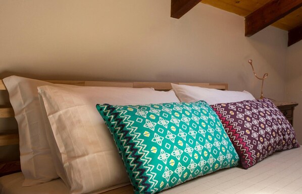 A bed with three pillows, two patterned and one plain, in a room with wooden beams on the ceiling. - B&B Casa Danoi (Trinita)