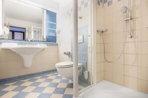 A bathroom with a checkered floor, a sink, a toilet, and a glass-enclosed shower area. - Hapimag Resort München (Munich)