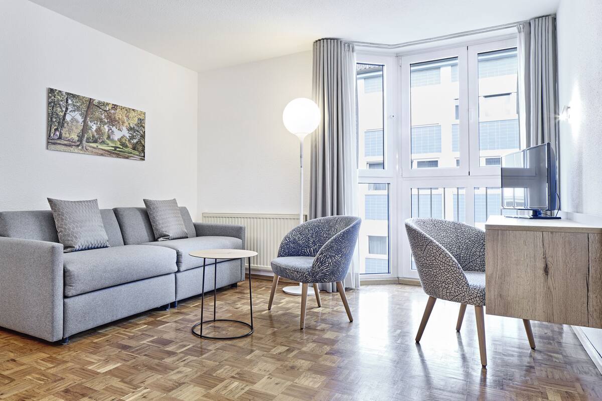 Un soggiorno moderno con un divano grigio, due poltrone a fantasia, un tavolino e un quadro appeso al muro.