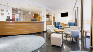 A modern hotel lobby with a reception desk, seating area, and a television screen. - Hapimag Resort München (Munich)