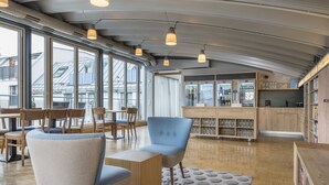 A modern interior with large windows, a bar area, and wooden furniture. - Hapimag Resort München (Munich)
