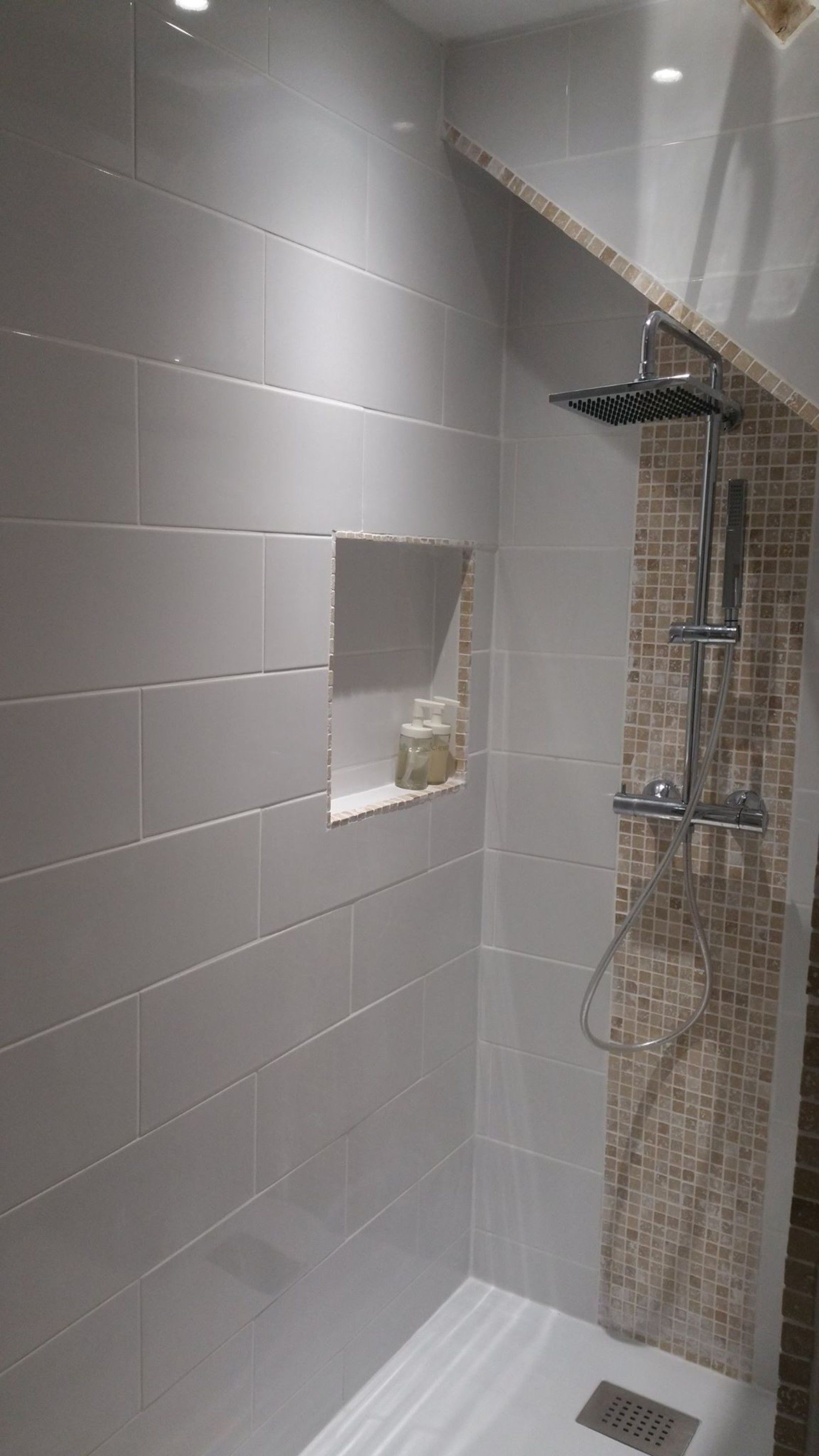 A shower area with grey tiles, a showerhead, and a small shelf with toiletries.