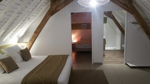 Ein Schlafzimmer mit schräg versiegelter Decke, einem Bett mit Kissen, einem Nachttisch und einer Hängeleuchte.