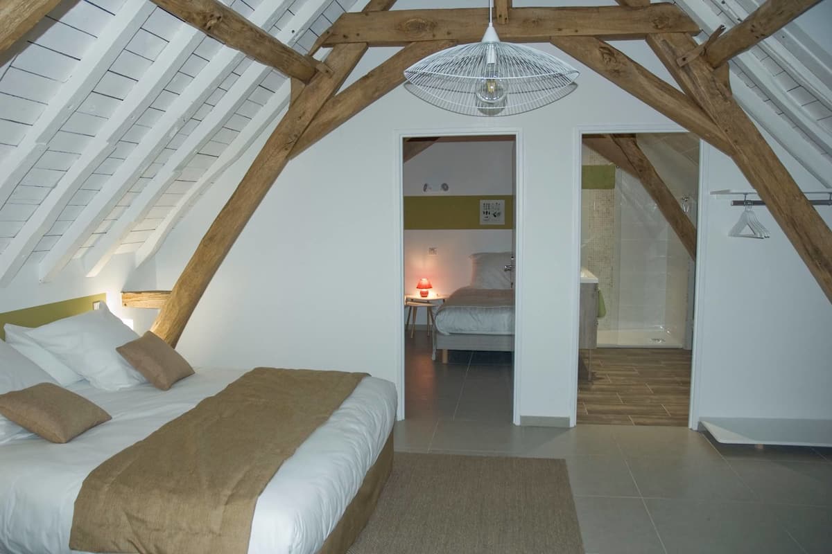 A bedroom with a sloped ceiling, a bed with white and brown bedding, a red lamp, and a wooden ceiling beam.