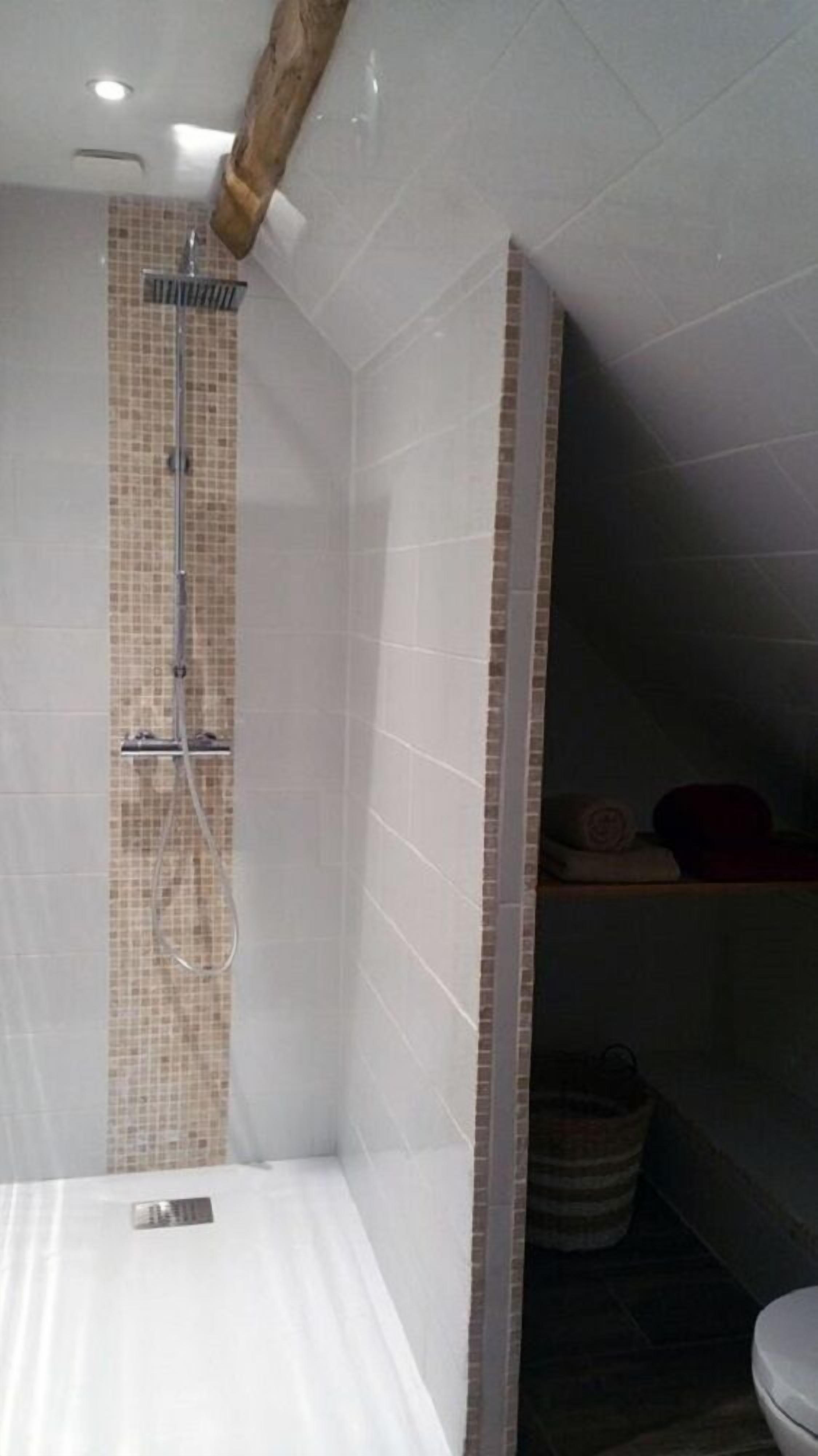 Une salle de bain avec une douche, des murs carrelés et un plafond avec une poutre en bois.