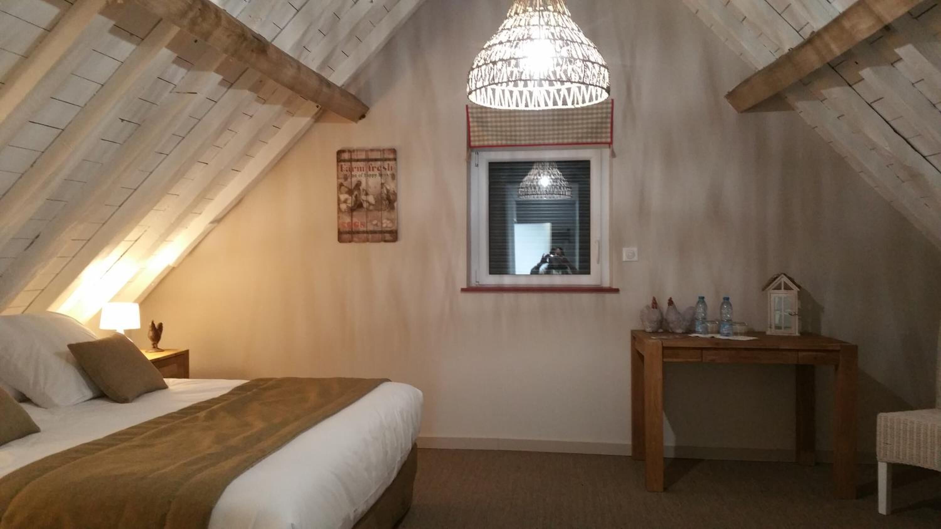 Een knus slaapkamer op zolder met een bed, een houten nachtkastje, een bureau en een hanglamp.