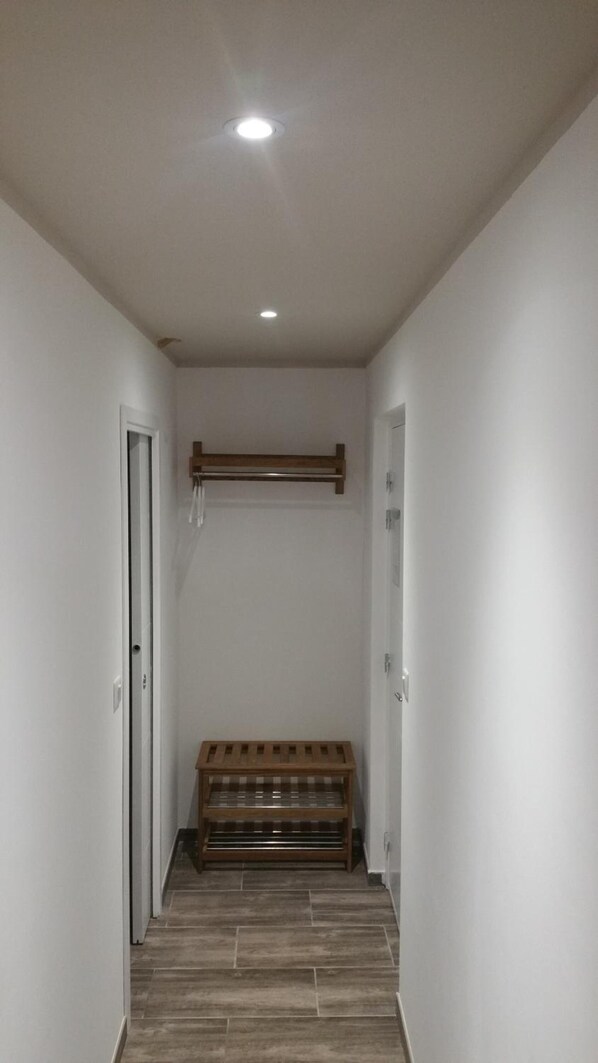 Un pasillo estrecho con un banco de madera, paredes blancas y una lámpara en el techo.