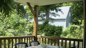 Un espace extérieur abrité, aménagé pour prendre les repas, avec une table dressée pour deux personnes, entouré de chaises, et offrant une vue sur un jardin avec des arbres et une maison en arrière-plan.