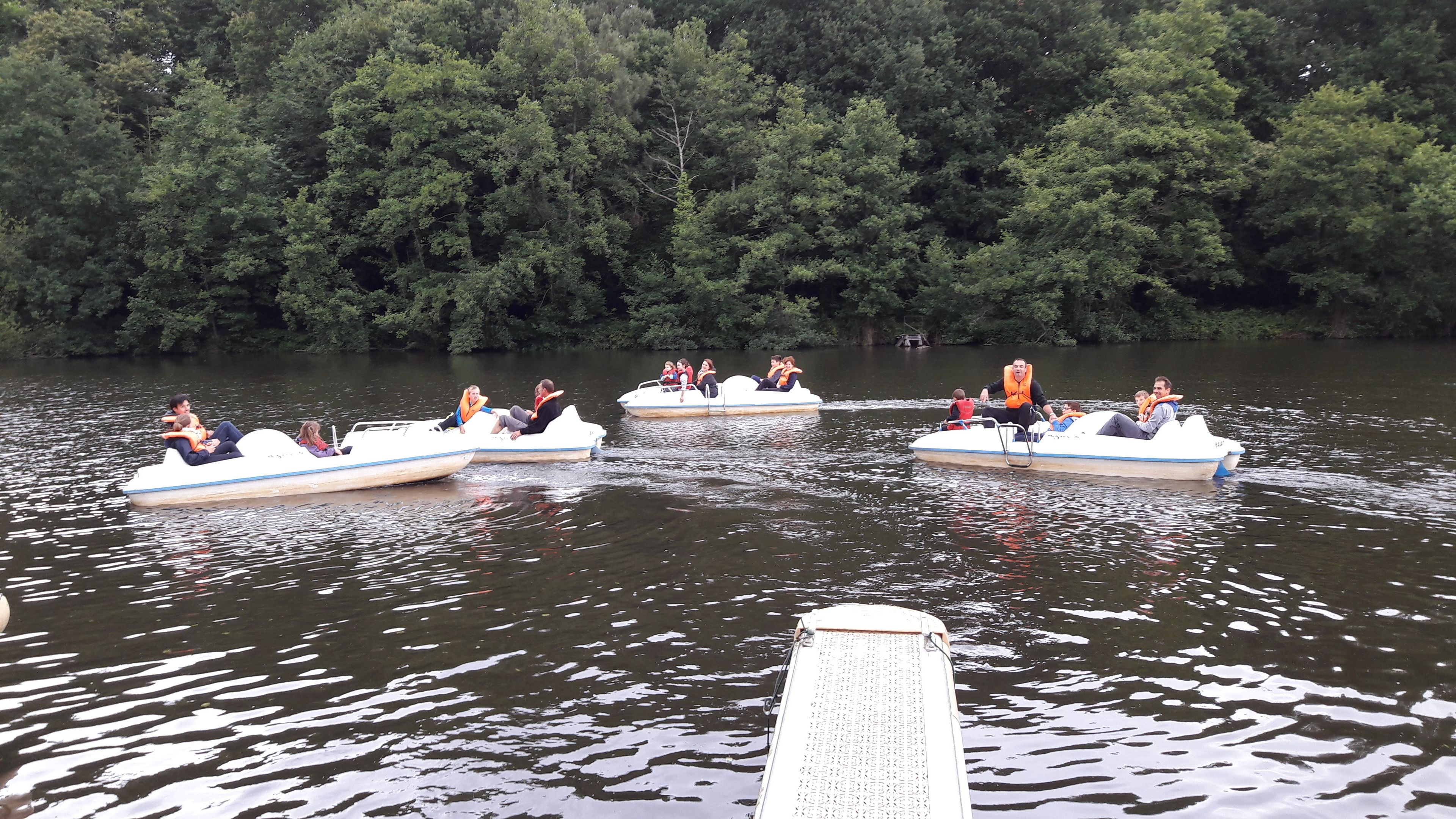 Trois petits bateaux sur un lac, avec des passagers portant des gilets de sauvetage.