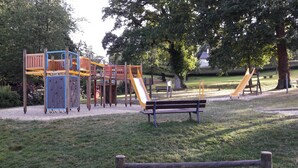 Une aire de jeux avec un toboggan, des structures d’escalade et un banc.